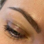 Nahaufnahme eines geschlossenen Auges mit langen Wimpern und einer natürlichen Augenbraue. Die Haut ist mit etwas Struktur und Poren sichtbar. Das Augenlid ist leicht mit neutralem Lidschatten bedeckt.